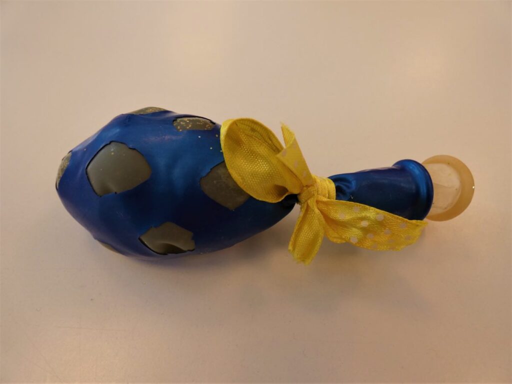 zdjęcie niebieskiego balonu z wyciętymi otworami, w środku żółty balon, całość związana żółtą tasiemką